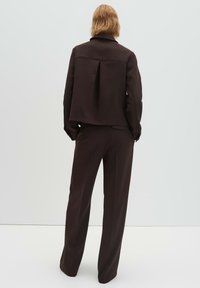 Bruin op maat gemaakt pak met een cropped blazer met plooidetail en bijpassende hoge taille broek. Glad materiaal met een gestructureerd ontwerp.