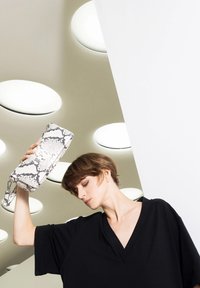 Snakeskin-patterned clutch bag in gray and white, with a detachable strap; held aloft against a modern, minimalist backdrop.