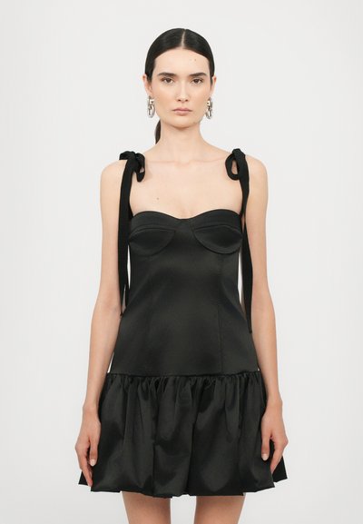Robe noire en satin, avec un corsage ajusté et une jupe volantr. Elle présente des bretelles en nœud et des bonnets moulés, créant une silhouette structurée.