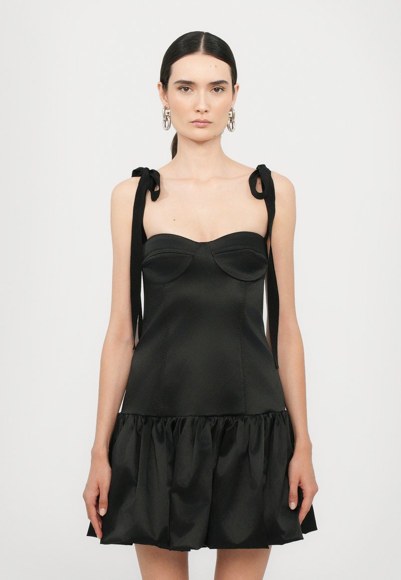 Vestido negro de tela satinada, con cuerpo ajustado y falda con volantes. Presenta tirantes tipo lazo y copas moldeadas, creando una silueta estructurada.