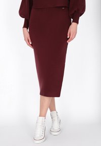Bordeaux midi-jurk met geribbelde textuur, met een slim-fit silhouet. Combinatie met witte hoge sneakers voor een casual uitstraling.