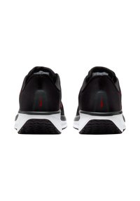 Zapatillas deportivas negras con parte superior de malla, acentos rojos y suela blanca. Incluyen un talón acolchado y una suela texturizada para tracción.