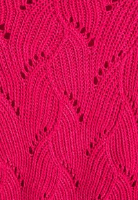 Rosa stickad tyg med ett vågmönster och öppna detaljer. Texturen är mjuk, med framträdande stygn och en livlig färg.