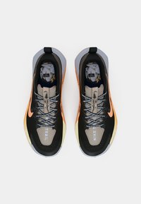 Een paar zwarte en oranje Nike trail hardloopschoenen met patroonveters en inlegzolen met een bos-thema, bekeken van bovenaf op een witte achtergrond.
