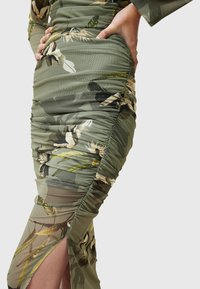 Abito verde con stampa floreale caratterizzato da una texture arricciata, maniche lunghe e uno spacco laterale. Realizzato in tessuto leggero e trasparente.