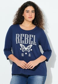 Navyblaues Langarm-T-Shirt aus weichem Material mit einem weißen Grafikdesign, das das Wort "REBEL" und einen Schmetterling zeigt, ergänzt durch Sterne.