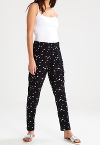 Černé kalhoty s uvolněným střihem, s bílým vzorem ptáků, elastickým pasem a měkkým materiálem. U páru s bílým tílkem a stříbrnými sandály.