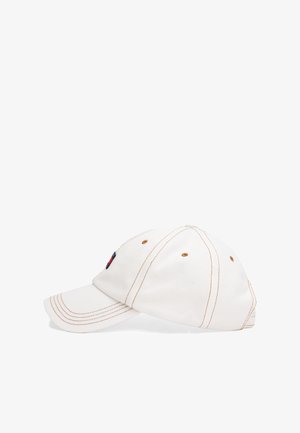 Balta kokvilnas beisbola cepure ar brūnām šuvēm, izliekta mala, izšūts logotips sānos un ventilācijas acs caurumi.