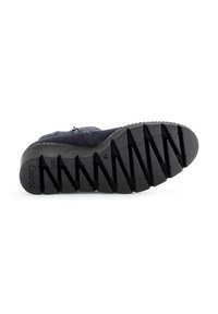 Semelle noire texturée d'une chaussure, présentant un motif de semelle en zigzag pour une meilleure adhérence. La botte a un design robuste avec des coutures visibles le long du bord.