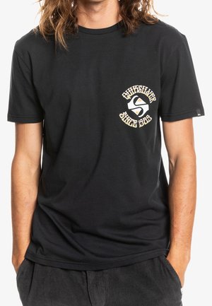 Zwart katoenen t-shirt met een beige afbeelding met de tekst "Quiksilver Since 1969" en een embleem op de linkerborst. Simpel ontwerp.