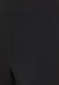 Närbild av svarta tygleggings som visar detaljerad sömnad längs insidan av låret och midjebandet.