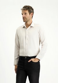 Camicia button-up chiara con una texture morbida, maniche lunghe e colletto classico, indossata con jeans di denim scuri.