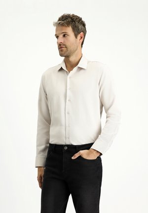 Camisa de botones de color claro con una textura suave, de mangas largas y un cuello clásico, llevada con jeans de mezclilla oscuros.