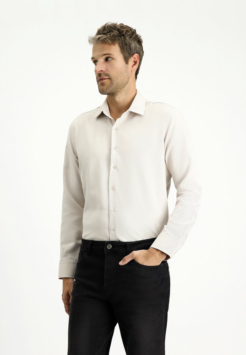 Camicia button-up chiara con una texture morbida, maniche lunghe e colletto classico, indossata con jeans di denim scuri.