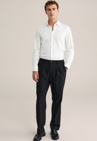 Camicia bianca a maniche lunghe con bottoni abbinata a pantaloni neri a pieghe e scarpe in pizzo nere, caratterizzata da una texture liscia e una vestibilità su misura.