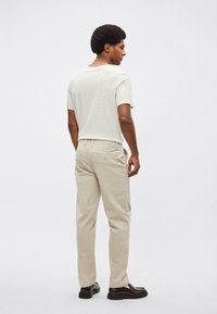 Μπεζ βαμβακερό μπλουζάκι, κοντά μανίκια, υφή με ανάγλυφο σχέδιο. Μπεζ παντελόνι κοτλέ, ίσια γραμμή, δύο πίσω τσέπες, φορεμένο με σκούρα παπούτσια.