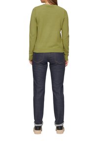 Grüner Pullover mit langen Ärmeln und rundem Ausschnitt, kombiniert mit dunkelblauen Jeans, die umgekrempelte Bündchen und Sneakers mit hellen Sohlen besitzen.