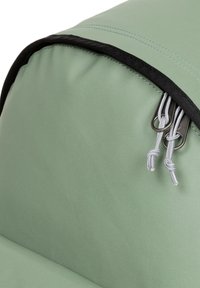 Bolsa de tela verde con una textura suave, ribete negro y accesorios de metal plateado. Presenta cuerdas y ganchos en el borde superior para el cierre.