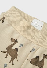 Beige tyg med ribbad midjeband; pryds med tryckta bruna kameler och blå kaktusar. Knapplåsning i midjebandet. Mjuk textur.