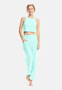 Ljus teal atletisk set som består av en ärmlös crop top och löst sittande byxor med fickor, tillverkad av ett mjukt, stretchigt tyg.