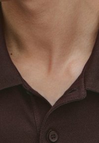 Ciemnobrązowa koszula z kołnierzykiem, z teksturowanej tkaniny, z zapięciem na dwa guziki i widocznym przeszyciem w okolicy kołnierza.