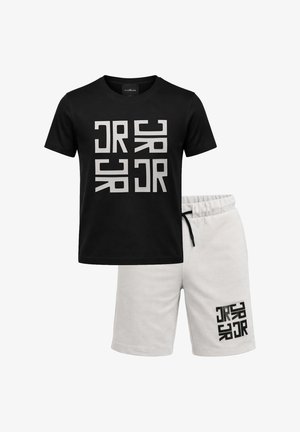 Maglietta nera a maniche corte con grande stampa geometrica astratta bianca, abbinata a pantaloncini grigio chiaro con coulisse e una stampa più piccola abbinate.