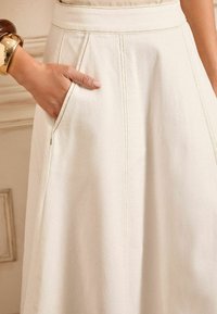 Licht beige rok met een gladde textuur, voorzien van zijzakken en zichtbare stiksels. De tailleband zit aansluitend en de stof lijkt duurzaam te zijn.