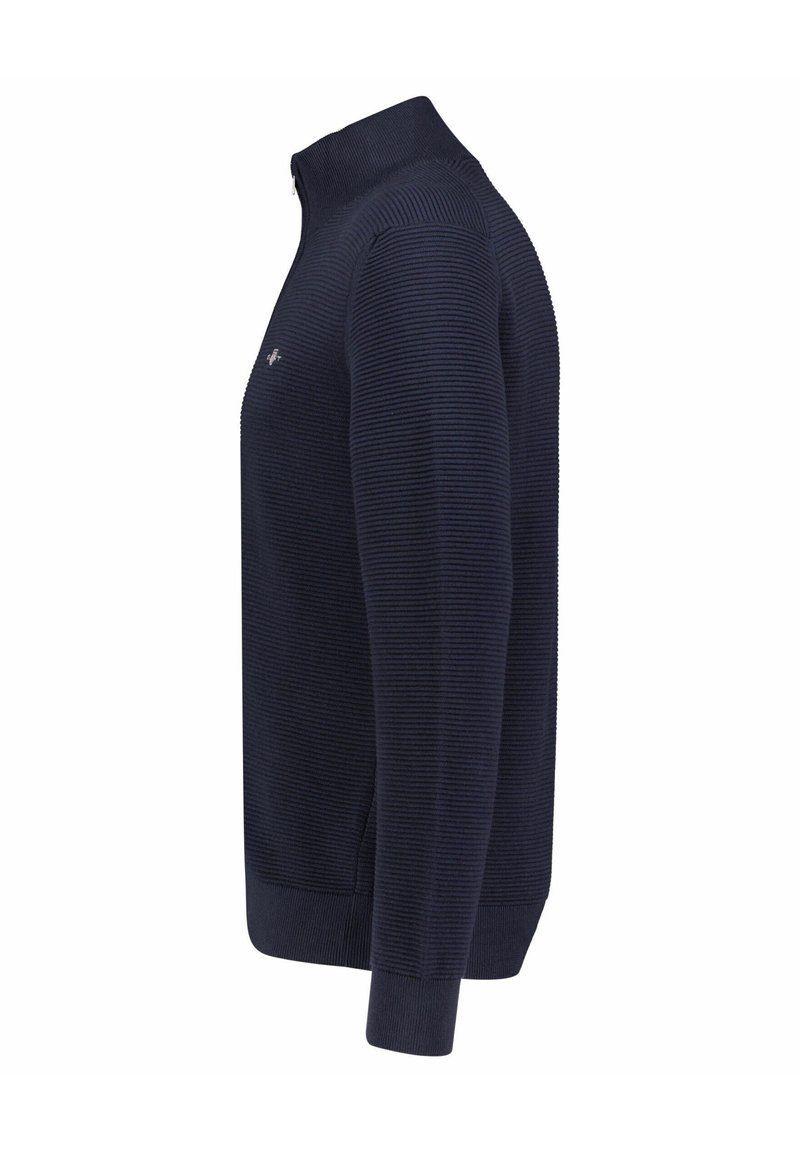 Marineblauer, gerippter Pullover mit langen Ärmeln, hohem Kragen und kleinem gesticktem Logo auf der Brust, seitlich dargestellt.