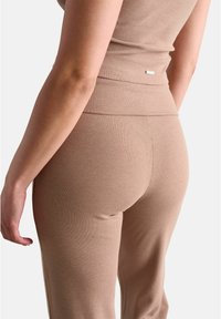 Brązowe prążkowane legginsy z wysokim stanem i małym metalowym akcentem logo. Materiał wydaje się miękki z pionową teksturą.