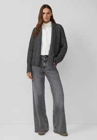 Grijze geribde cardigan met brede mouwen, gedragen over een witte blouse met kraag en gecombineerd met hoge grijze jeans, met een losvallende pasvorm en een afgesneden zoom.