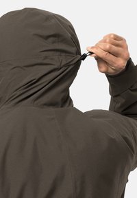 Brun hættejakke med en struktureret finish, der har en justerbar snor. Visningen viser en hånd, der justerer snoren ved halsen.