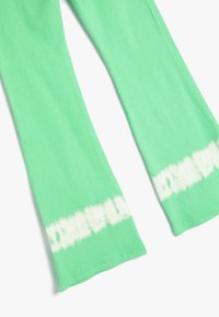 Groene geribde legging met een uitlopende vorm en een wit tie-dye patroon aan de zoom. Zacht materiaal met elastische stof voor comfort.