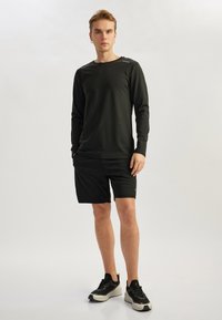 Camiseta deportiva de manga larga negra y pantalones cortos negros, hechos de tejido que absorbe la humedad. Presenta un cuello redondo y sutiles detalles reflectantes. Zapatillas negras.