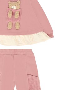 Roze sweatshirt met een geribbelde berenzak, gelaagd met een crèmekleurige ruffle; bijpassende roze broek met zijzakken en een textuurafwerking.