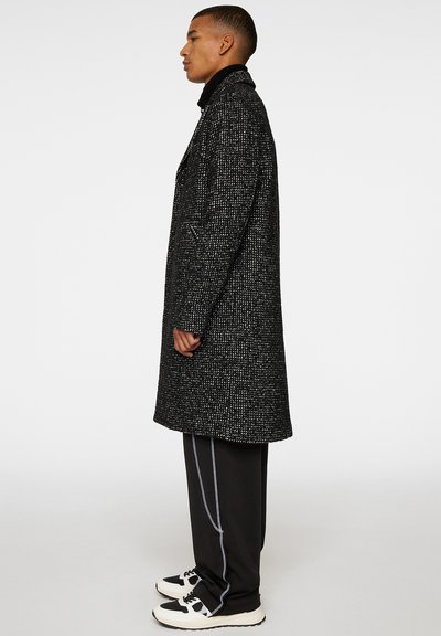 Zwart-wit houndstooth jasje met een op maat gemaakte uitstraling, zijzakken en een hoge kraag, gedragen over zwarte broek en witte sneakers, gezien vanaf de zijkant.