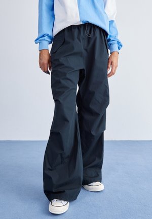 Pantalones negros de pierna ancha hechos de una tela ligera, con una cintura elástica y bolsillos laterales, combinados con zapatillas blancas.