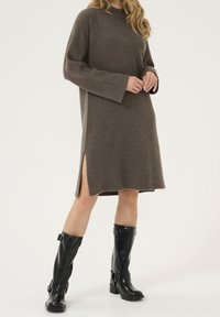 Brun ribbad stickad klänning med långa ärmar, sidoklipp och avslappnad passform, tillsammans med svarta glansiga knähöga stövlar med remmar.