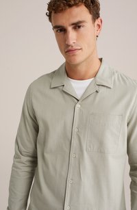 Svetlozeleni srajčni zgornji del iz mehkega materiala, ki ima klasičen ovratnik, žep na prsih in preprost, čist dizajn.