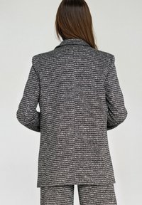 Czarnobiała marynarka w kratę w jodełkę z usztywnionym kołnierzem, pojedynczym rozcięciem i dopasowanym krojem. Teksturowana tkanina o profesjonalnym wykończeniu.