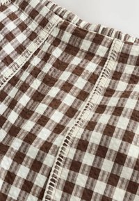 Tissu à carreaux marron et blanc avec taille élastique et détails de coutures décoratives verticales.