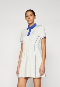 Short-sleeve white polo dress with a blue collar and vertical pleats at the waist, accented by purple stitching and logo on the chest.
