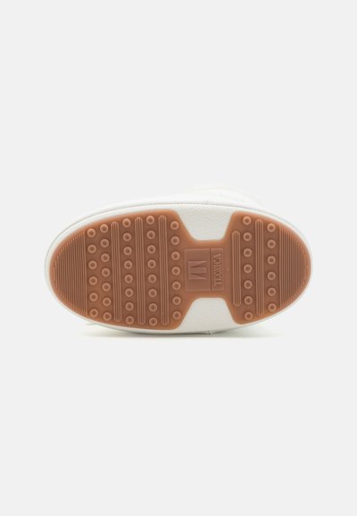 Hvit sneaker såle med en teksturert brun gummiyttersåle som har sirkulære grep og rektangulære seksjoner for grep. Rent, minimalistisk design.