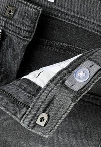 Primer plano de la cintura de unos vaqueros gris oscuro que muestra el botón, la cremallera y la etiqueta de cuidado de la tela en el interior de la cintura.