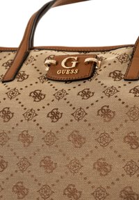Beige canvas håndtaske med et geometrisk præg mønster, brune læderdetaljer og hardware i guldtoning med et logo-plade.