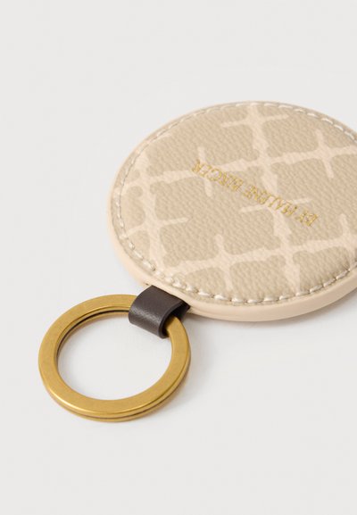 Porte-clés rond en cuir beige avec motif texturé, bords cousus, texte doré, attaché à un anneau en métal doré par une boucle en cuir foncé.