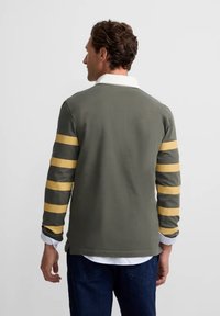 Camisa polo de manga larga en color verde oliva con rayas amarillas en las mangas; cuenta con un collar blanco y un corte relajado.