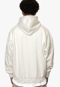 Hoodie oversize blanc en tissu doux avec une grande capuche, une taille élastiquée et des épaules tombantes ; texture lisse, design simple.