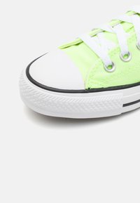 Primo piano di una sneaker in tela verde neon con punta in gomma bianca, lacci bianchi e suola bianca texturizzata su uno sfondo chiaro.