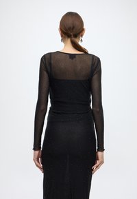 Fekete, hosszú ujjú ruha átlátszó anyagból, finom, csillogó részletekkel díszítve. Testhez simuló szabású, mélyített hátú.