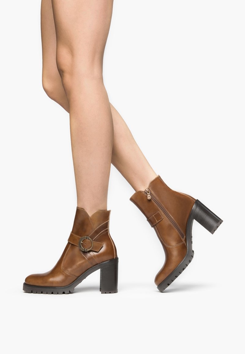 Bruine leren enkellaarsjes met een gestapelde hak, voorzien van een decoratieve band en ronde gesp. De zool heeft een textuur met een robuust ontwerp.